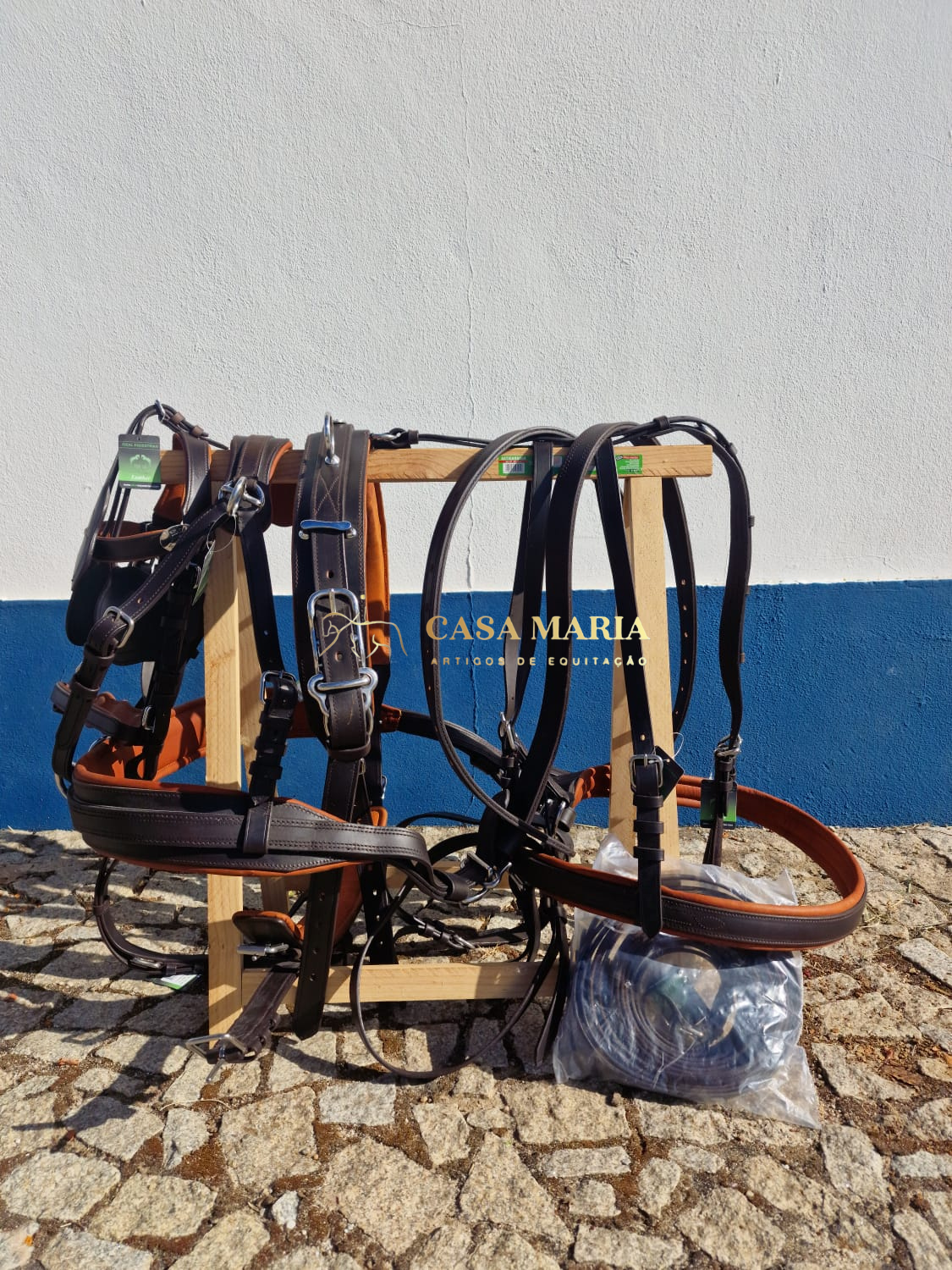 Selas e arreios de couro pendurados em estrutura de madeira com parede branca e azul ao fundo