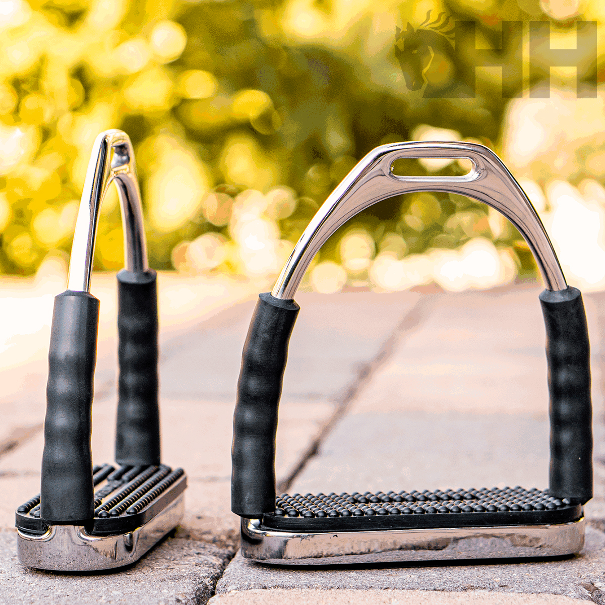 Par de estribos de montar metálicos com borracha preta e textura antiderrapante, colocados no chão exterior.