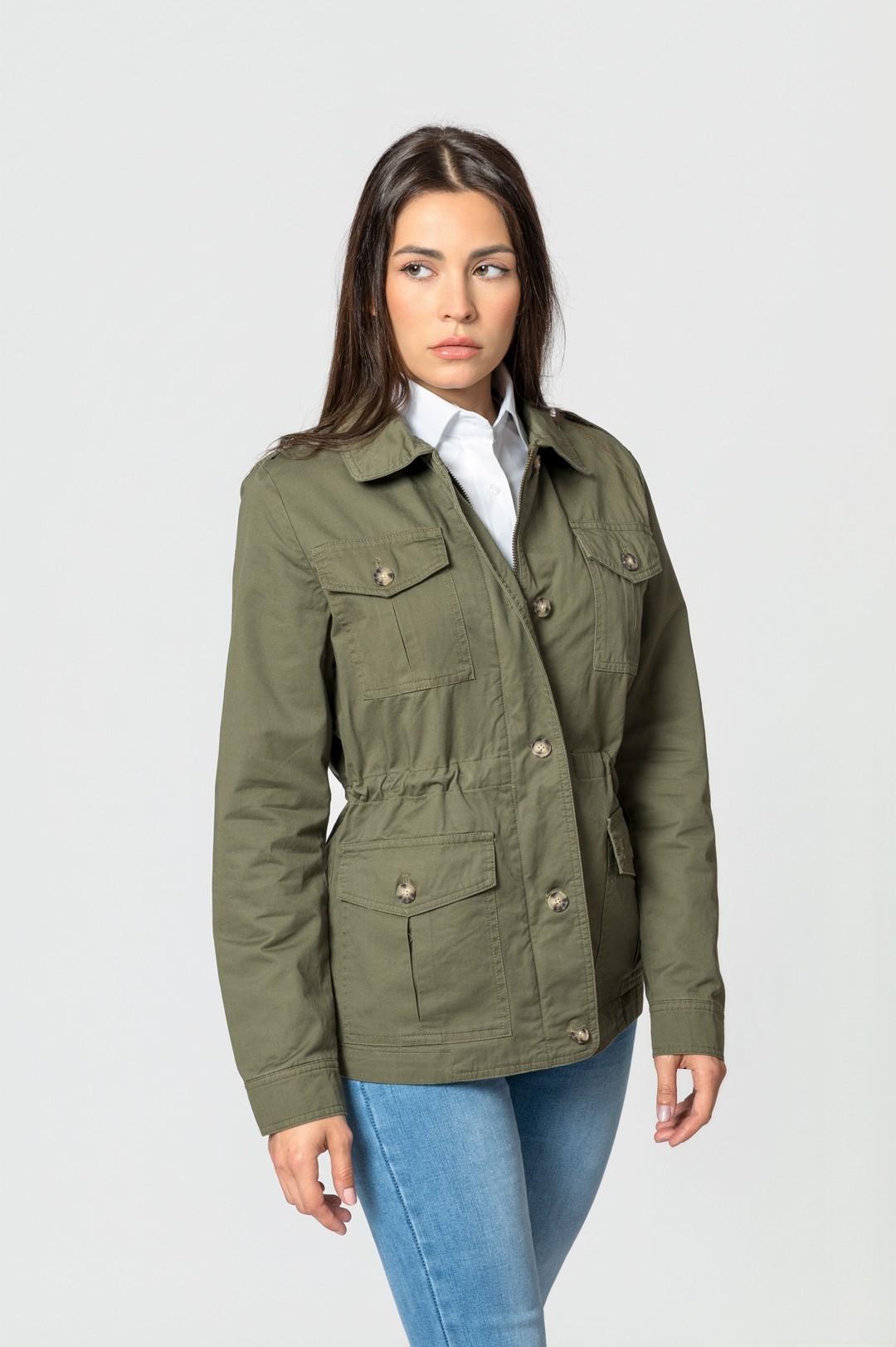Casaco verde militar feminino com botões e bolsos, usado com camisa branca e jeans azul.
