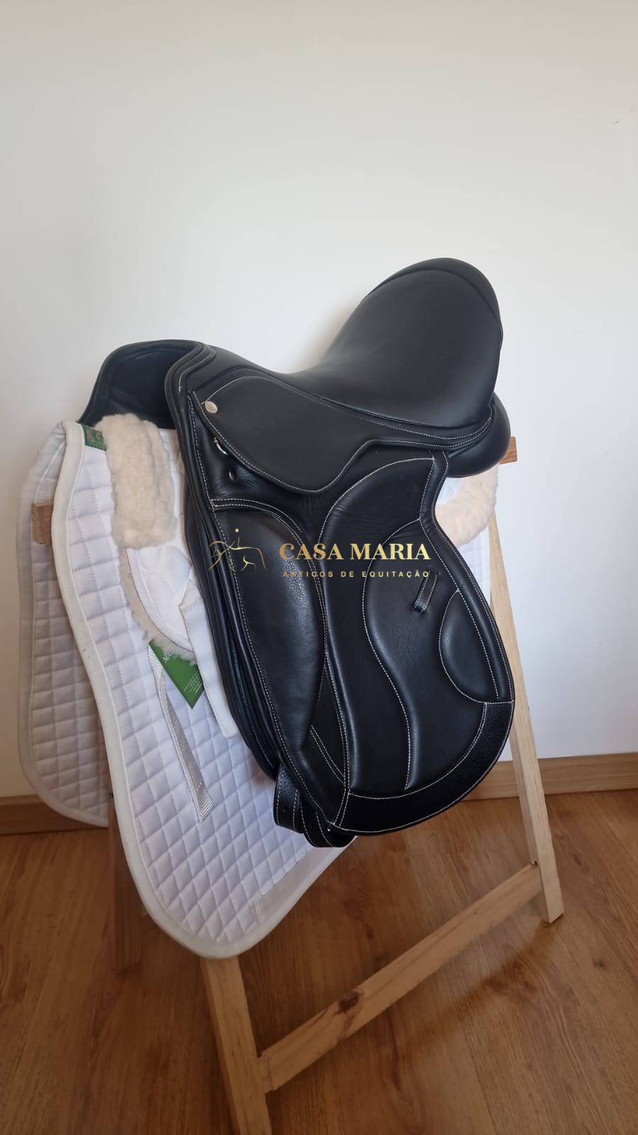 Sela preta de couro em suporte de madeira com mantilha branca acolchoada.