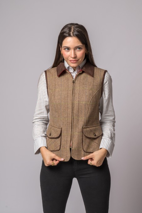 Colete castanho tweed com bolsos e gola castanha usado com camisa branca xadrez e calças pretas.