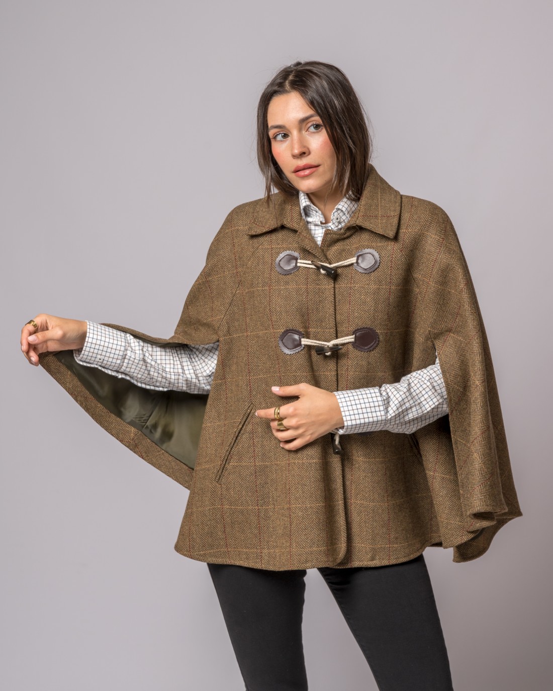 Mulher a usar capa castanha com padrão risca de giz e alamares, com camisa quadriculada branca e cinza.