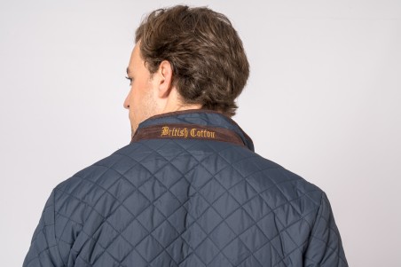 Casaco matelassado azul escuro com gola castanha e texto 'British Cotton'