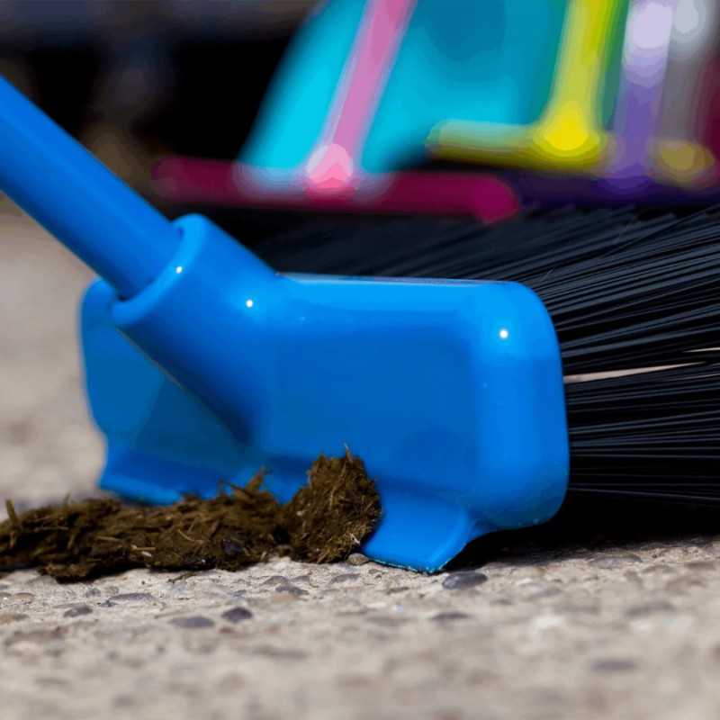 Vassoura e pá azul a varrer detritos castanhos num chão de pedra