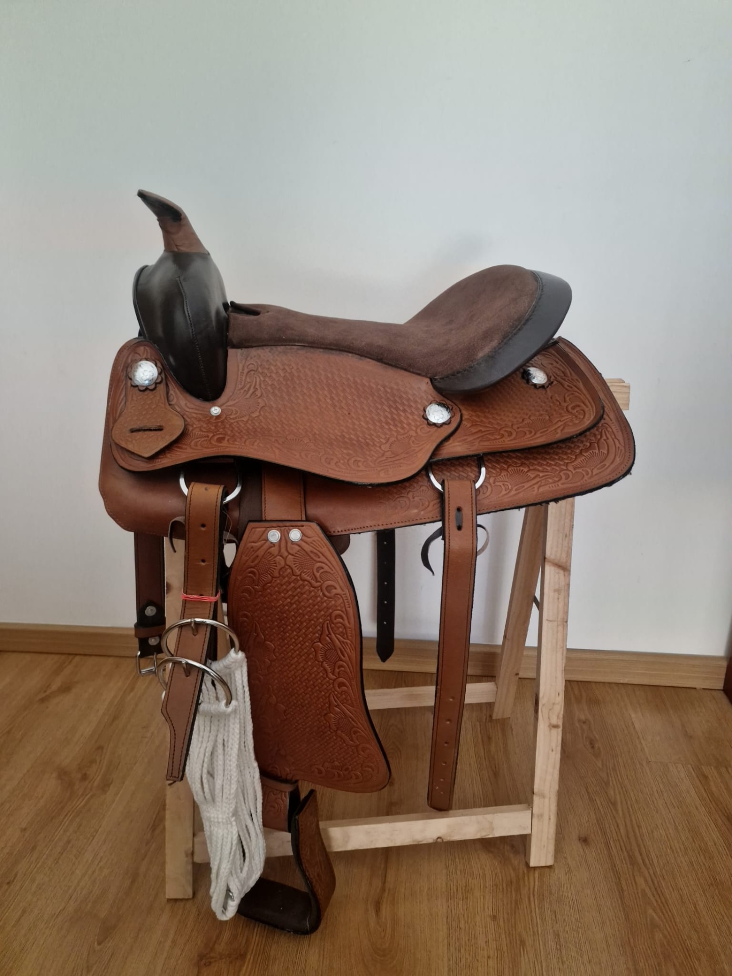 Sela de cavalo de couro castanho com assento acolchoado castanho escuro em suporte de madeira