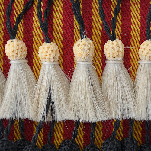 Franjas de corda branca com bolas bege trançadas sobre tecido vermelho, amarelo e preto