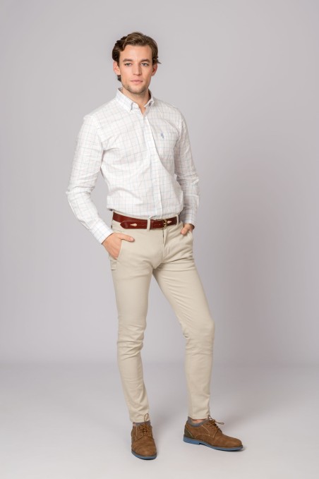 Homem com camisa branca de linhas, calças bege, cinto e sapatos castanhos em fundo cinzento