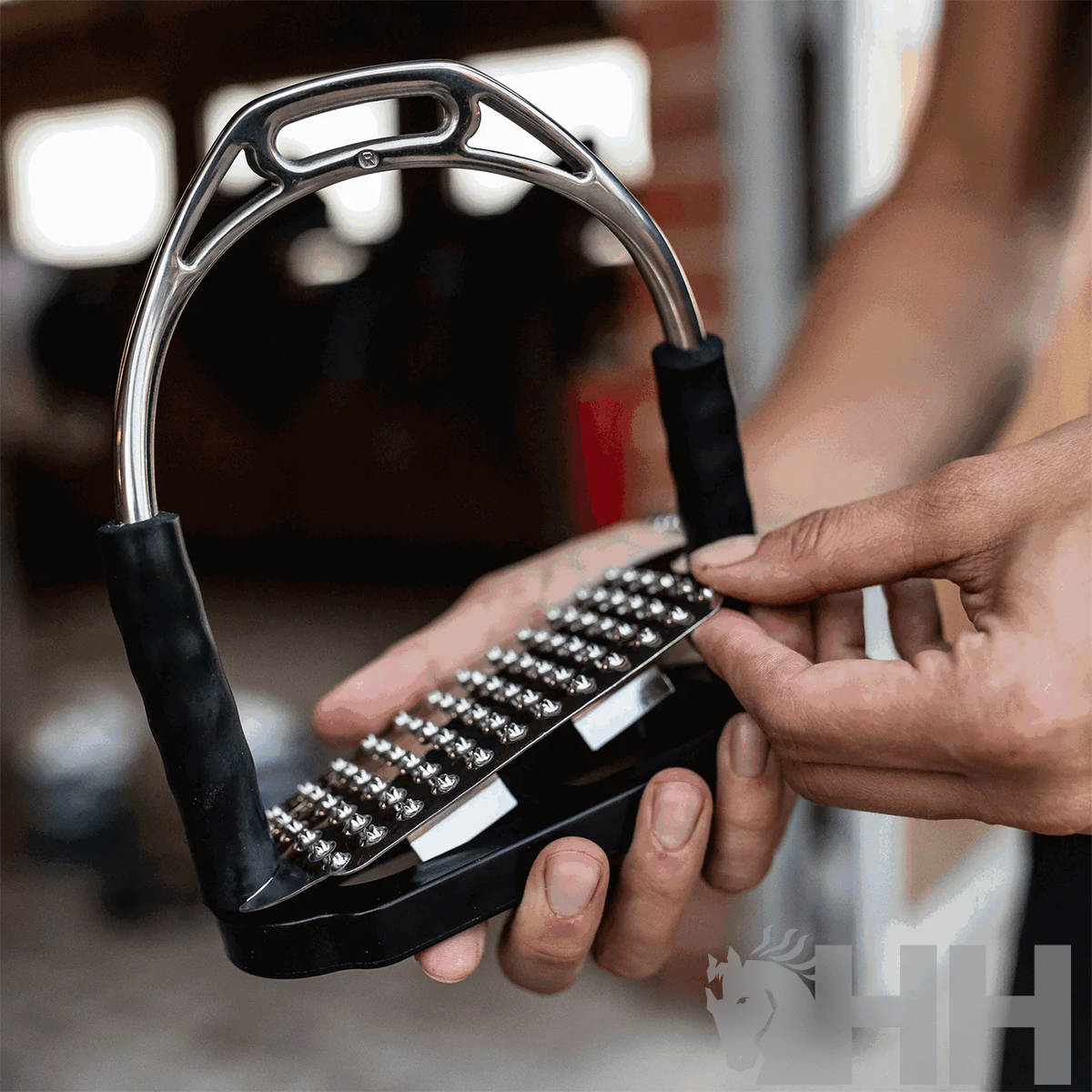 Estribo de equitação metálico com revestimento preto e base texturizada a ser segurado por uma mão