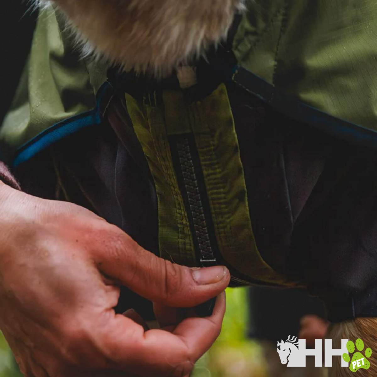Mão a fechar fecho de roupa verde com pêlo na gola e logótipo HH