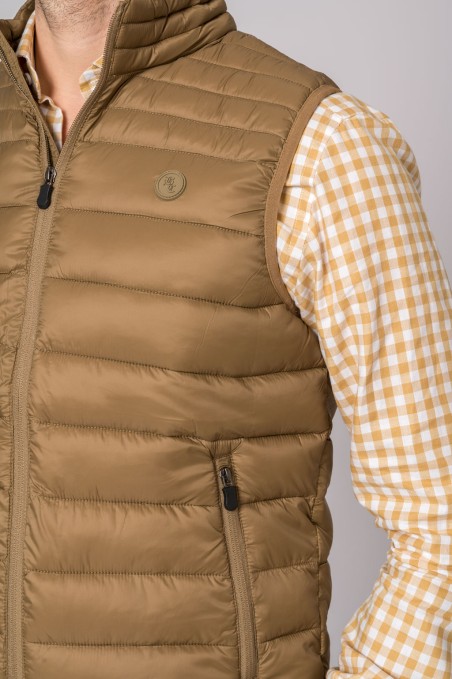 Colete masculino bege acolchoado usado sobre camisa xadrez branca e bege