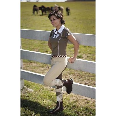 Mulher com roupa de equitação junto a vedação branca em campo gramado.