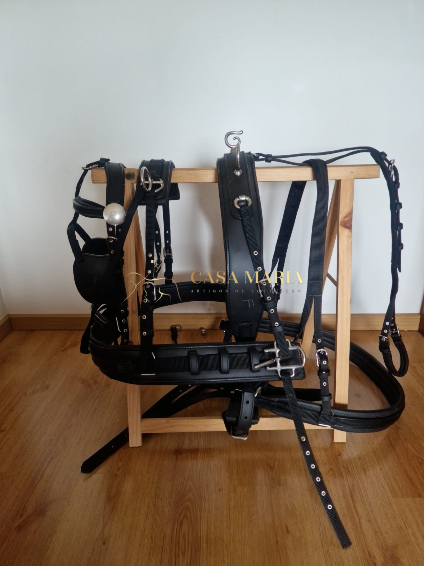 Arreio de cavalo preto em couro pendurado em suporte de madeira