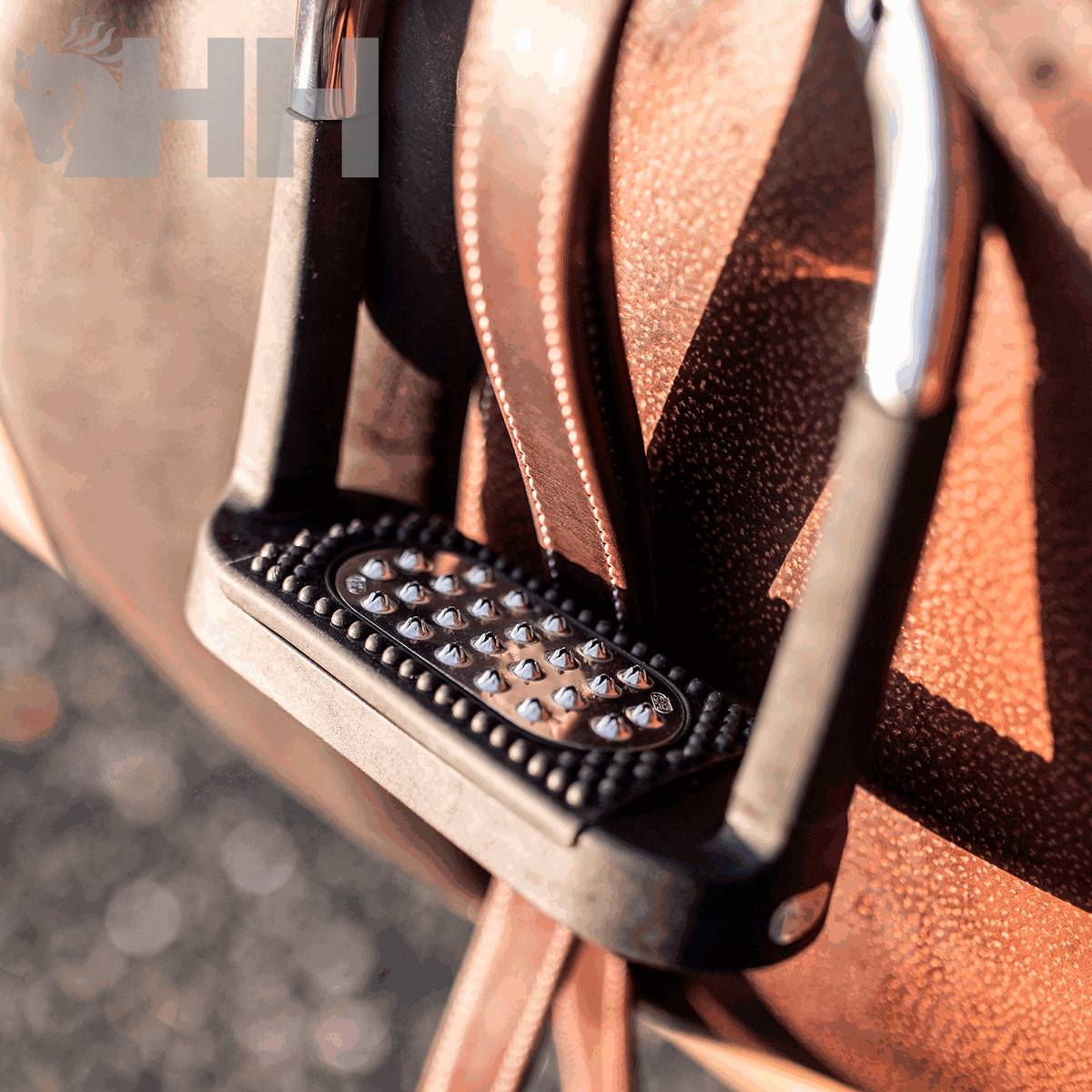 Estribo metálico com base preta antiderrapante pendurado numa sela de pele castanha