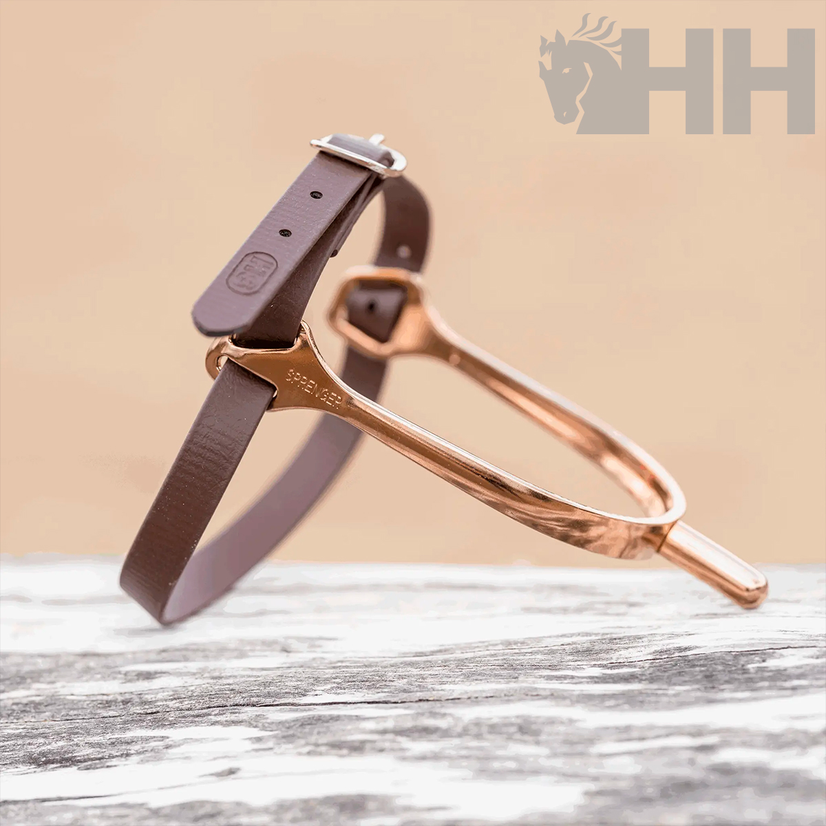 Espora rosa dourada com correia de couro castanha sobre superfície de madeira clara