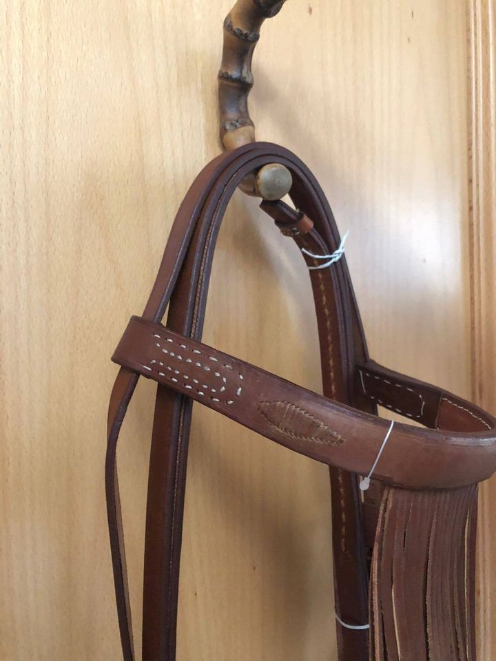 rédeas em couro castanho com franjas penduradas numa parede de madeira