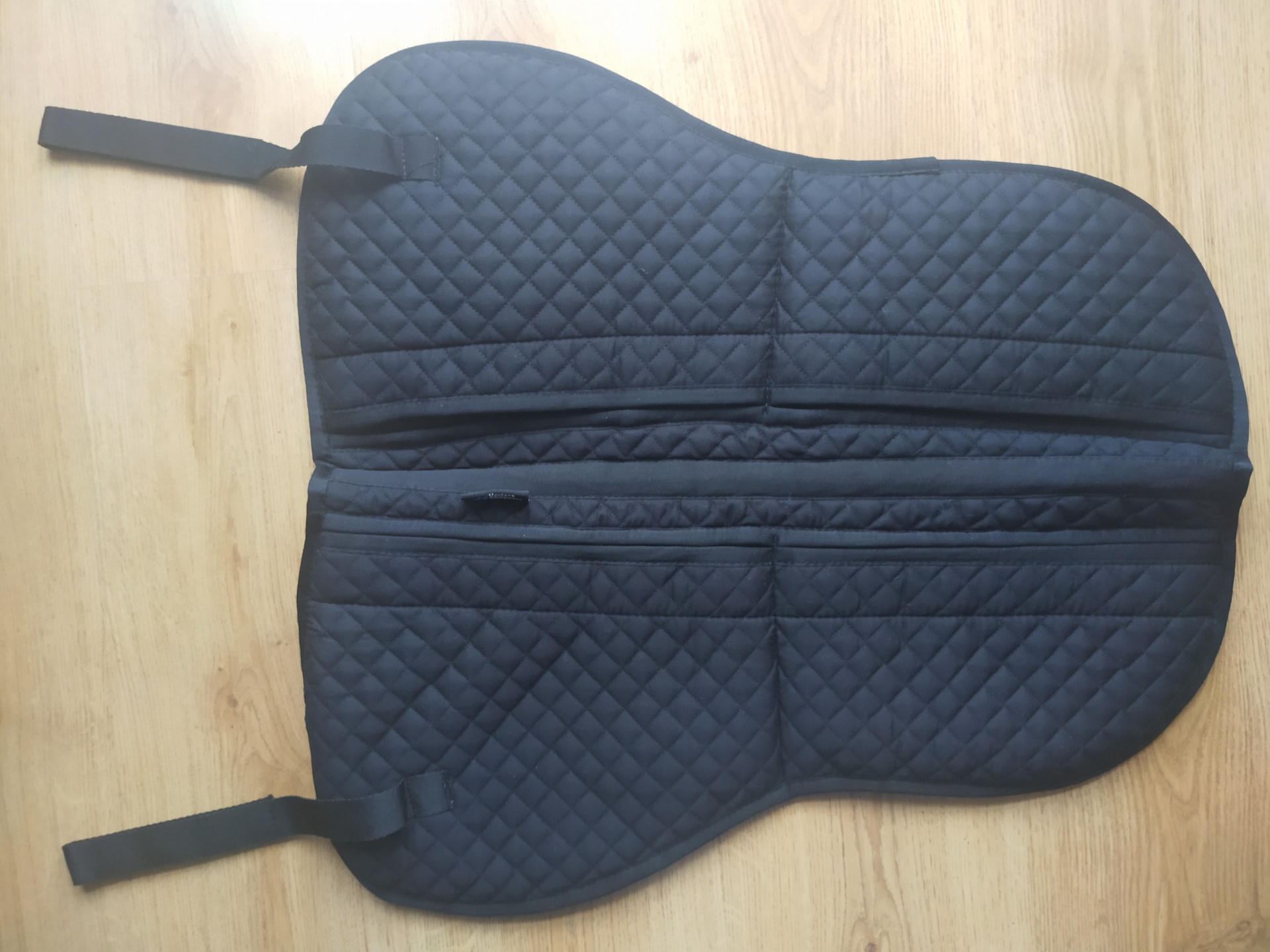 Peça acolchoada preta com padrão de losangos sobre chão de madeira clara