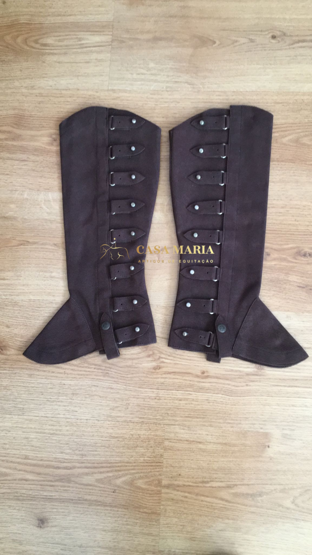 Par de polainas castanhas em tecido com tiras e botões sobre piso de madeira