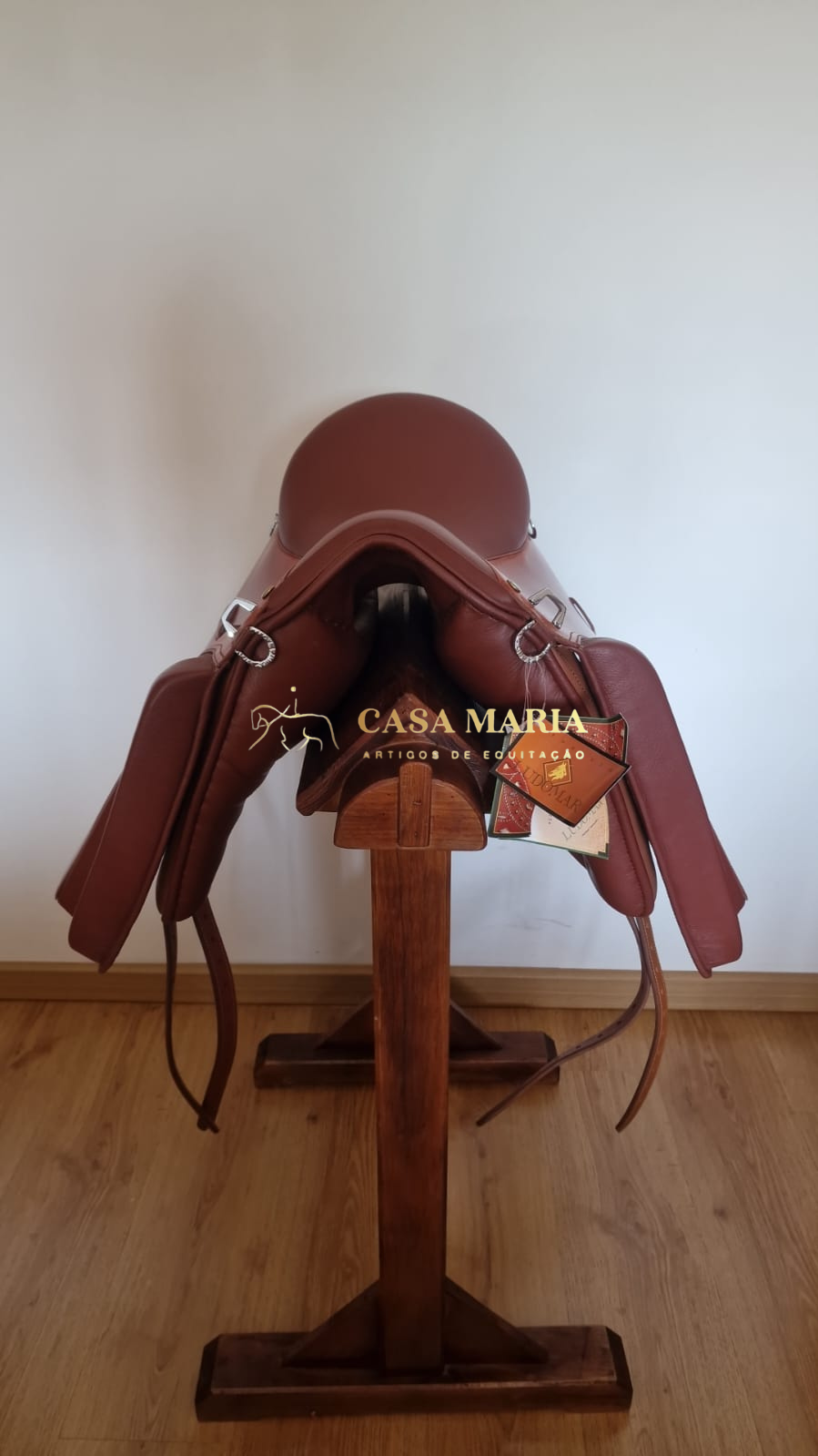 Sela de equitação em couro castanho escuro sobre suporte de madeira