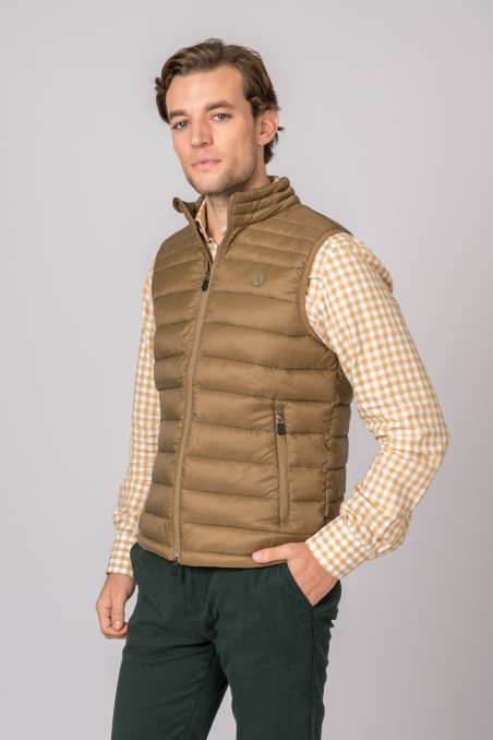 Colete acolchoado castanho com fecho, sobre camisa xadrez bege e branco, calças verdes escuras