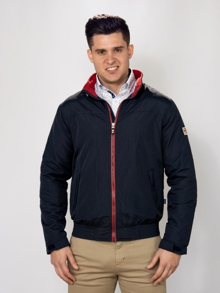 Homem a vestir casaco preto com fecho vermelho e camisa branca com padrão azul