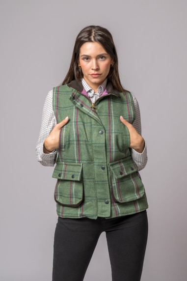 Colete verde aos quadrados com dois bolsos frontais e botões, usado por mulher com camisa branca e calças pretas