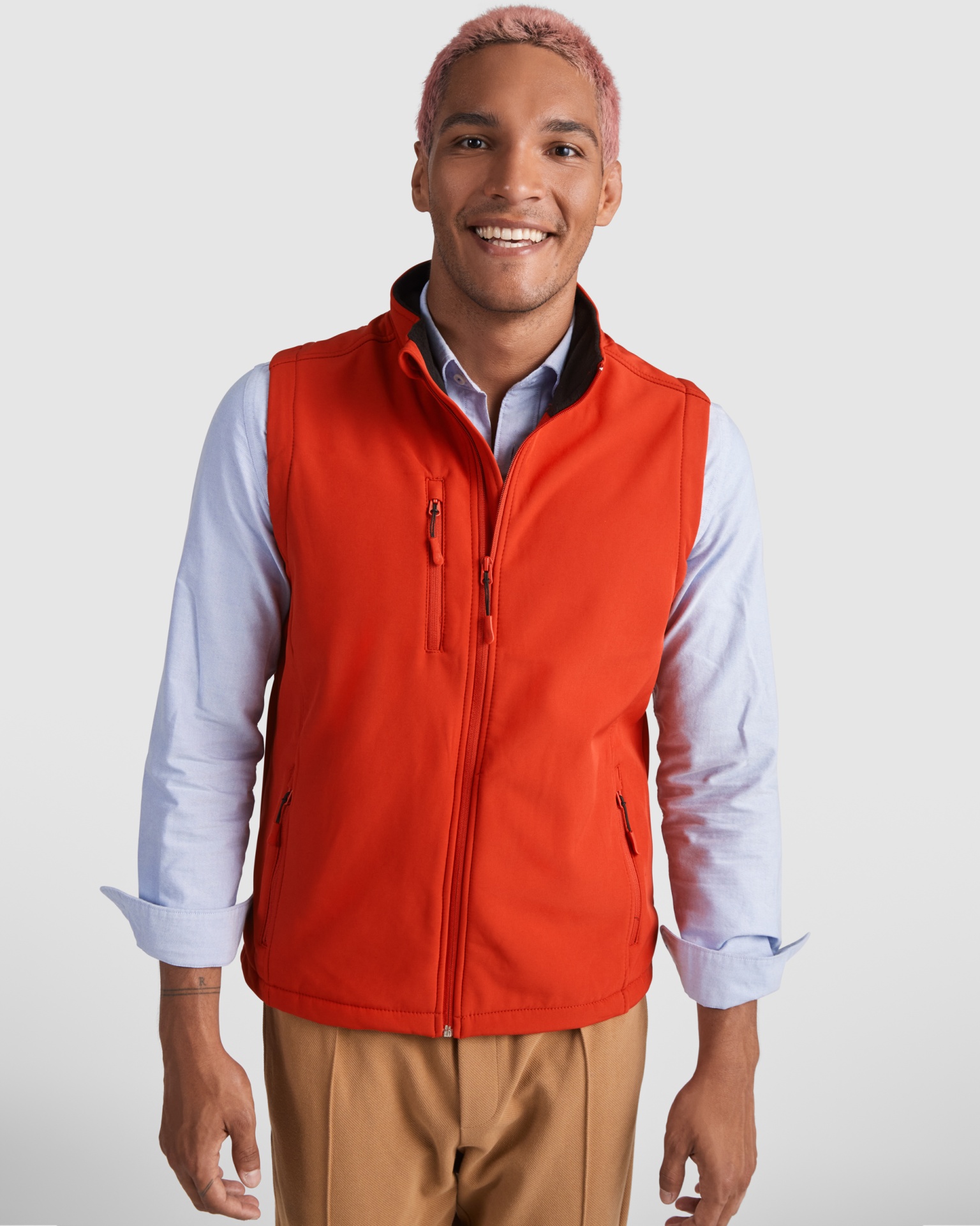 Homem com colete vermelho sobre camisa azul clara e calças beges