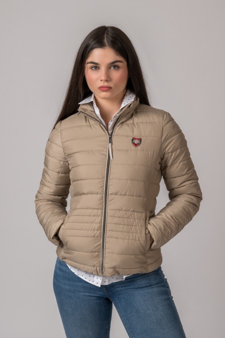 Mulher a vestir casaco bege acolchoado com fecho e emblema e camisa branca com padrão e jeans azuis