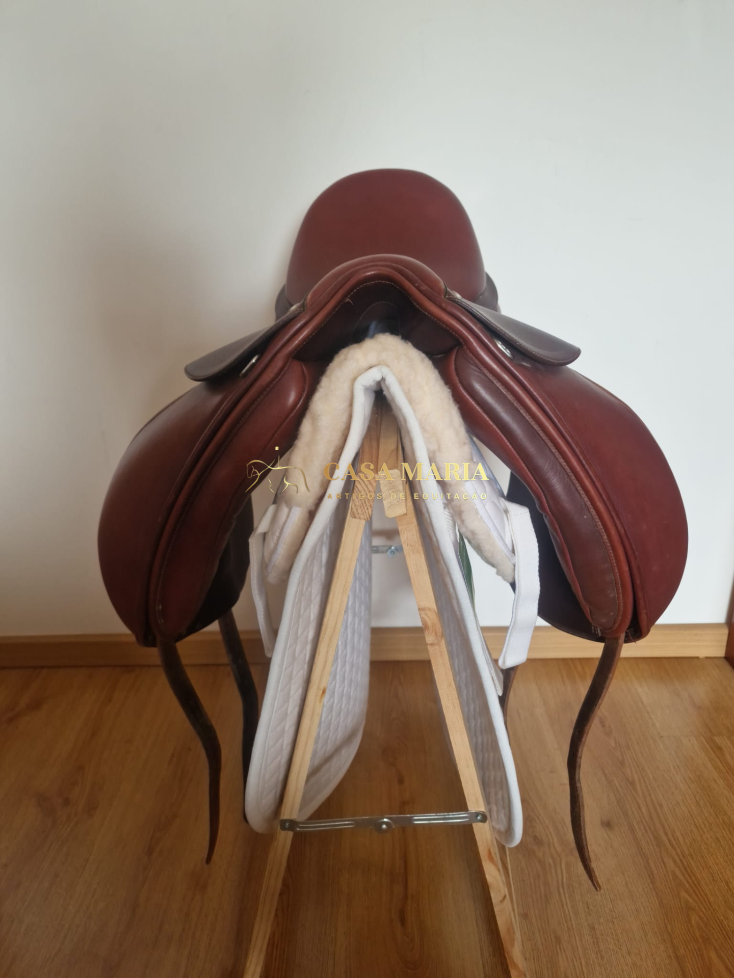 Sela de equitação em couro castanho em suporte de madeira com acolchoamento branco.