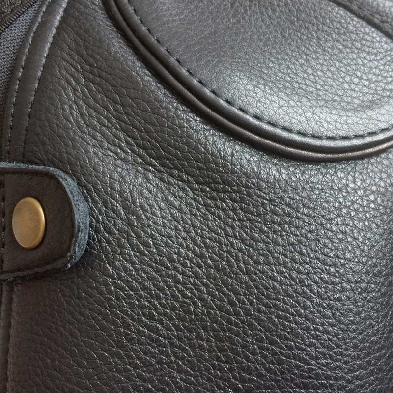 Superfície de couro preto com botão metálico dourado e costuras visíveis