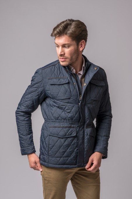 Homem a usar casaco azul escuro matelassê com bolsos e botões sobre camisa e calças bege