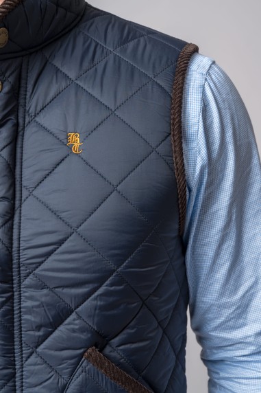 Colete acolchoado azul escuro com bordas castanhas e logotipo BT amarelo