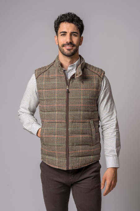 Homem com colete xadrez castanho e camisa branca com padrão posando