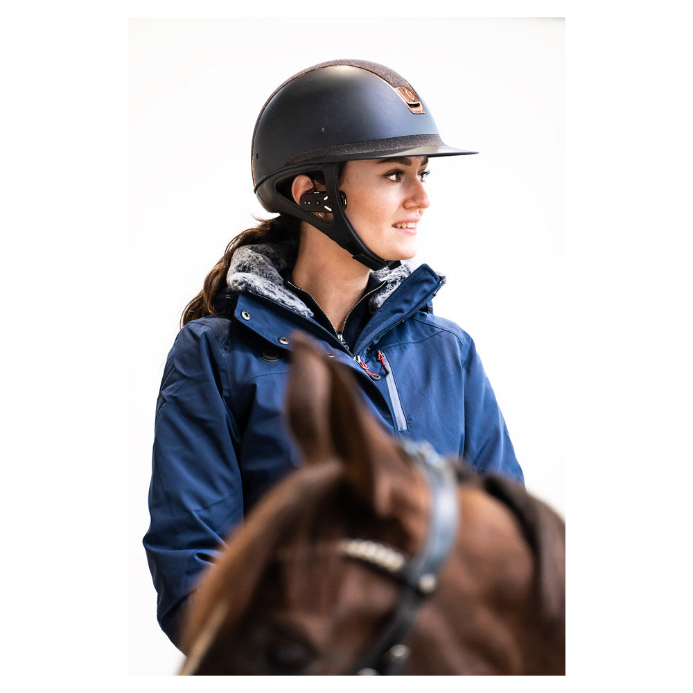 Mulher com capacete preto e casaco azul montando cavalo castanho