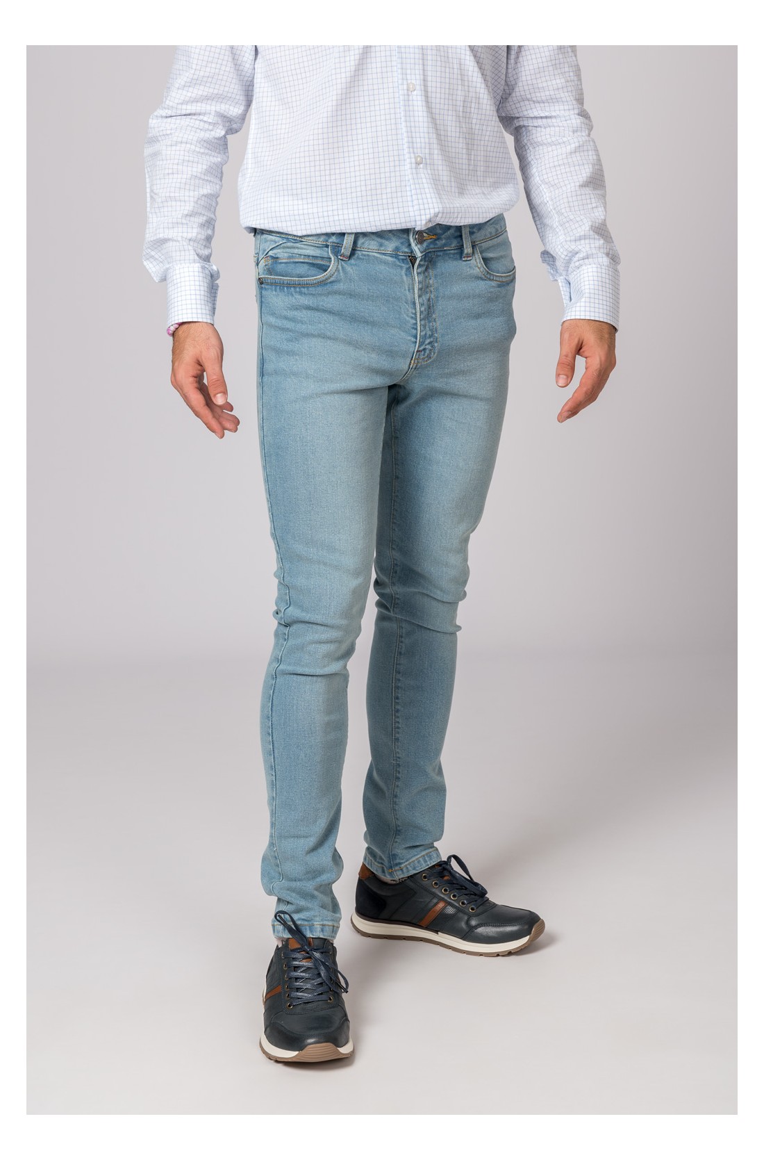 Homem com calças de ganga azul claro, camisa branca padrão e sapatos desportivos pretos