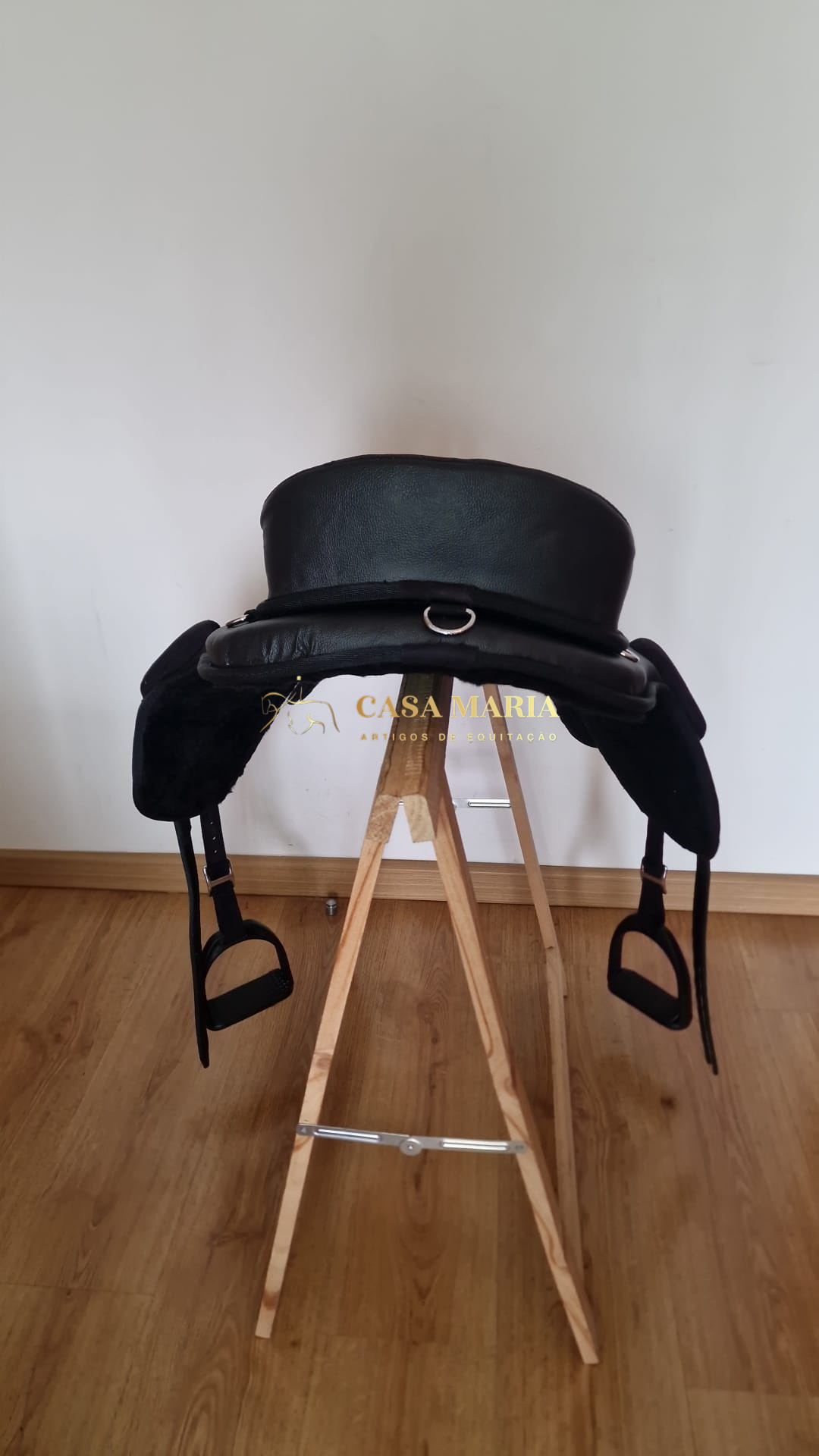 Sela de equitação preta em tripé de madeira com texto CASA MARIA em dourado