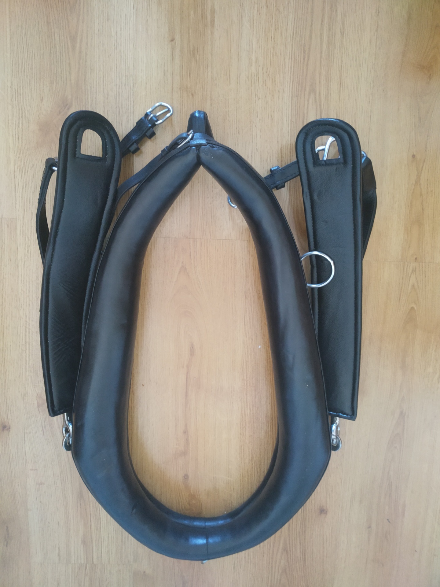 Puxador de couro preto com metais, colocado sobre piso de madeira clara.