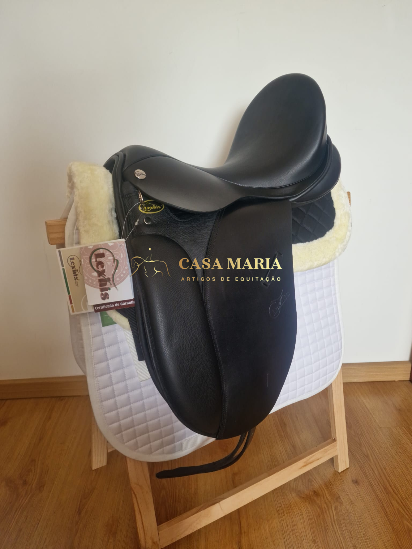 Sela de equitação preta sobre manta branca e cinza em suporte de madeira