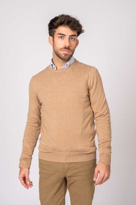 Homem com camisola bege de malha e calças cáqui, camisa azul clara, fundo branco.