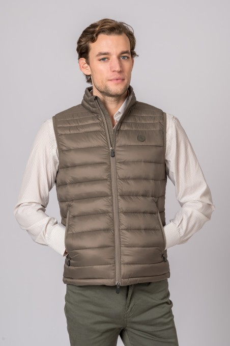 Homem a usar colete acolchoado castanho claro com camisa branca e calças verdes