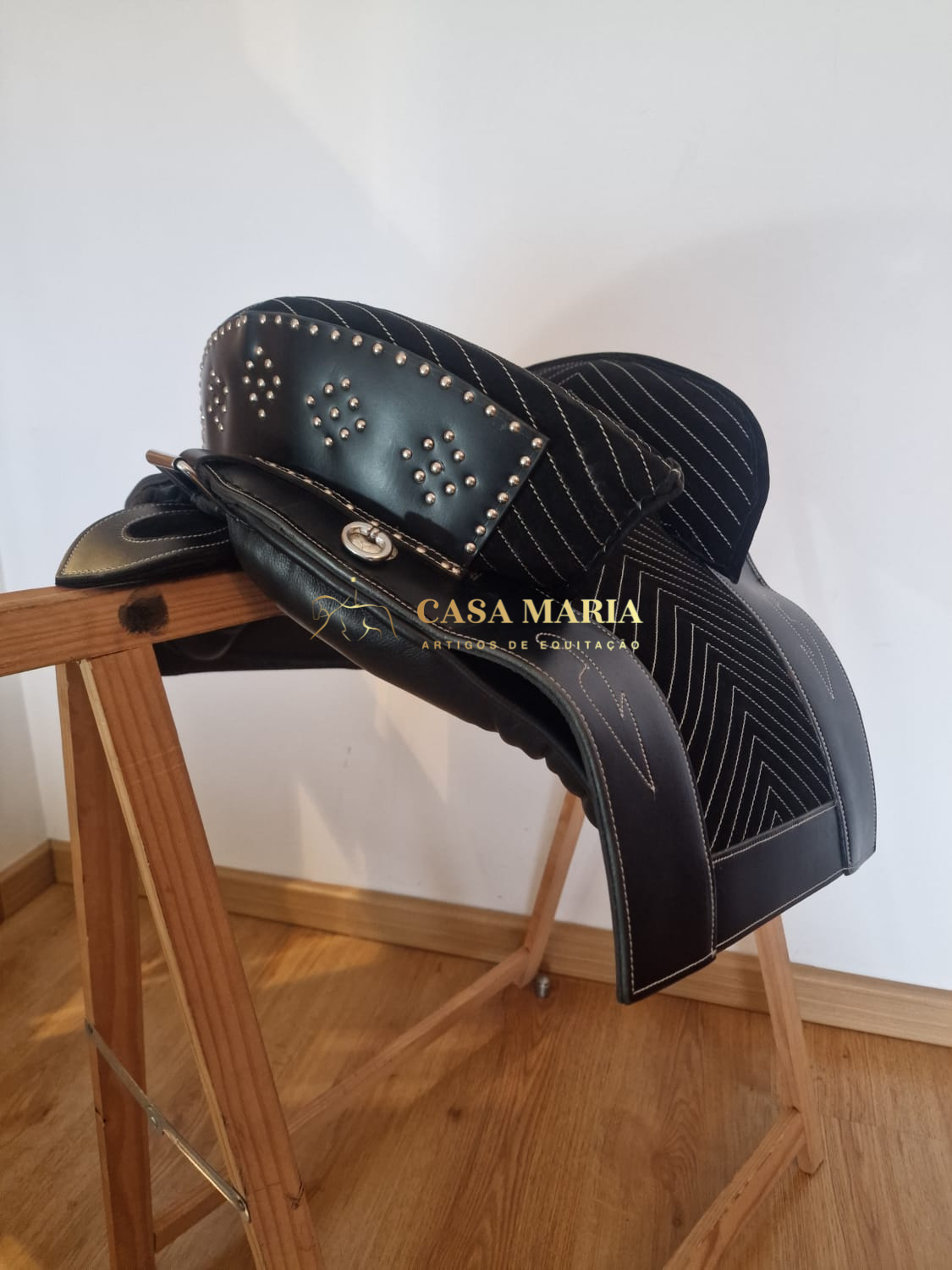 Sela de equitação preta com detalhes metálicos em suporte de madeira
