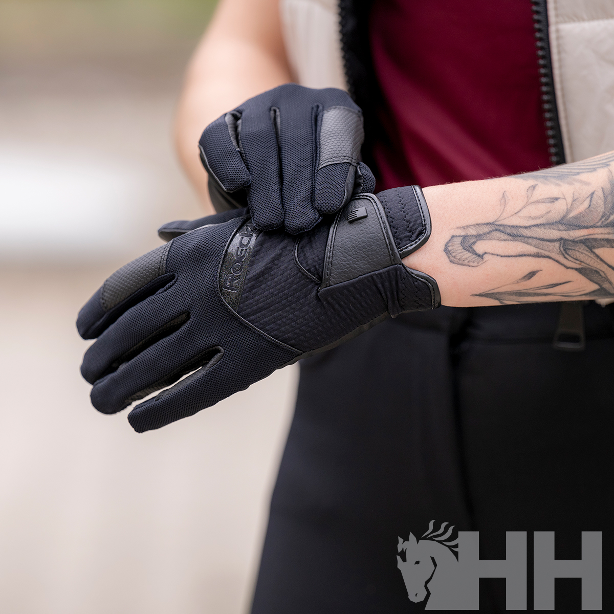 Luvas pretas com detalhes texturizados em uso por pessoa com tatuagem no antebraço