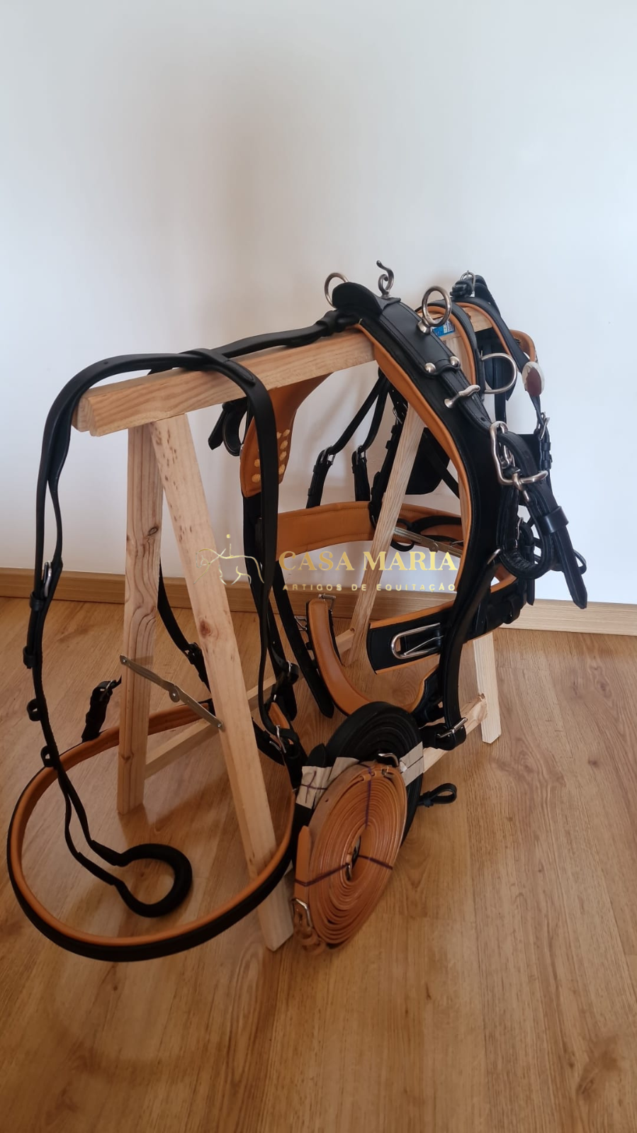 Peça de arreio para cavalo em couro preto e castanho com fivelas metálicas, sobre estrutura de madeira