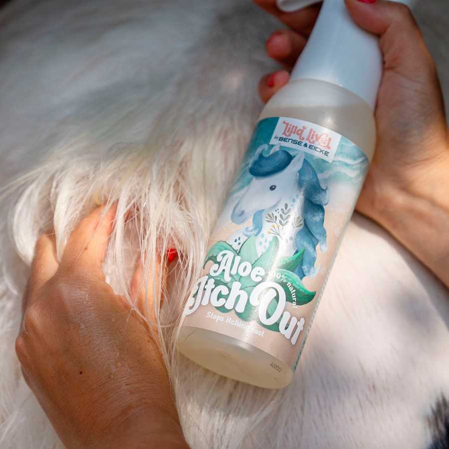 Frasco de spray com rótulo de cavalo azul e texto Aloe Itch Out segurado junto a cão branco.