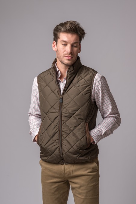 homem a usar colete matelassê castanho com fecho e bolsos, camisa quadriculada e calças bege
