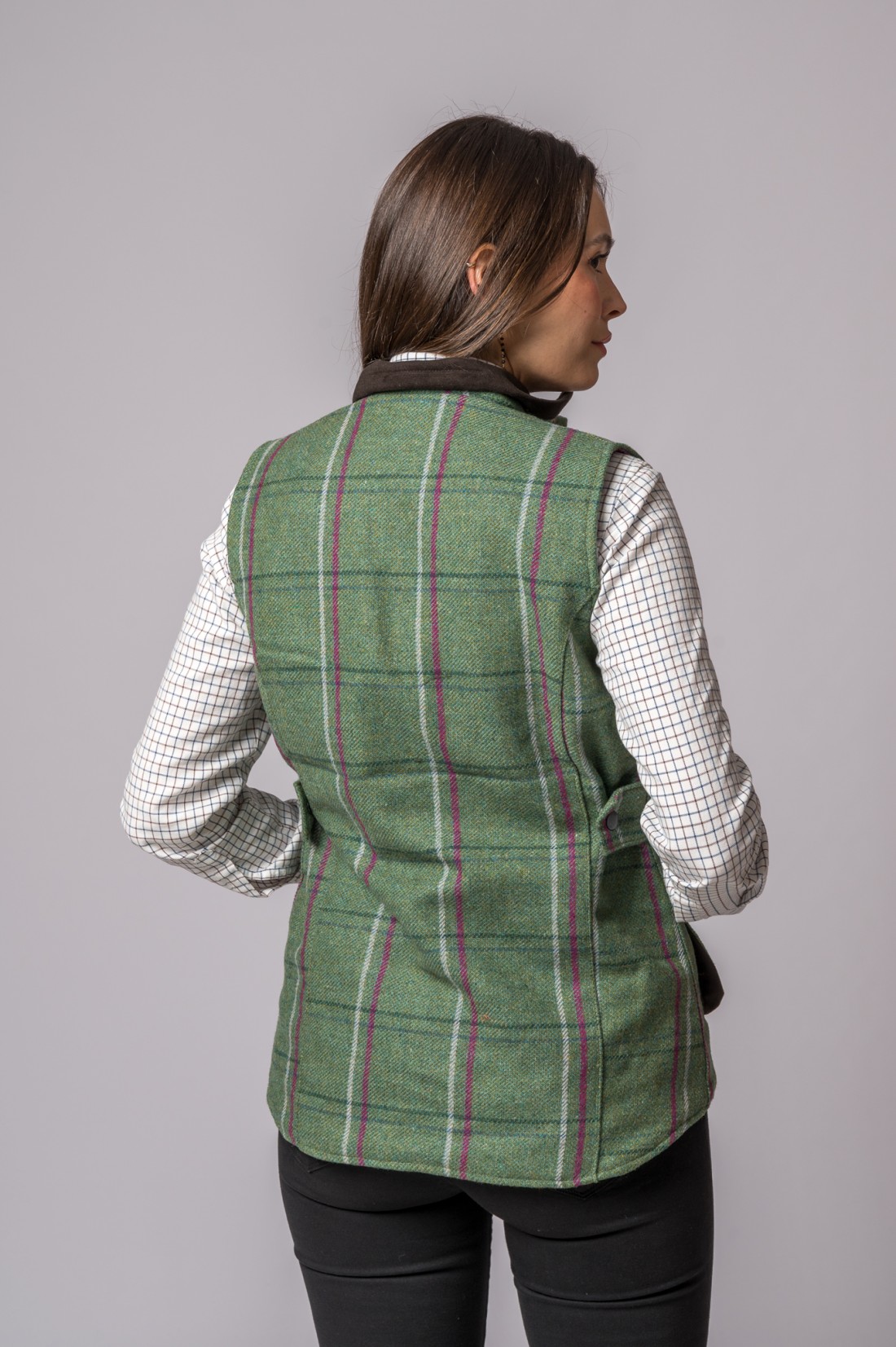 Colete verde riscado em tweed com camisa quadriculada branca usada por mulher vista de costas