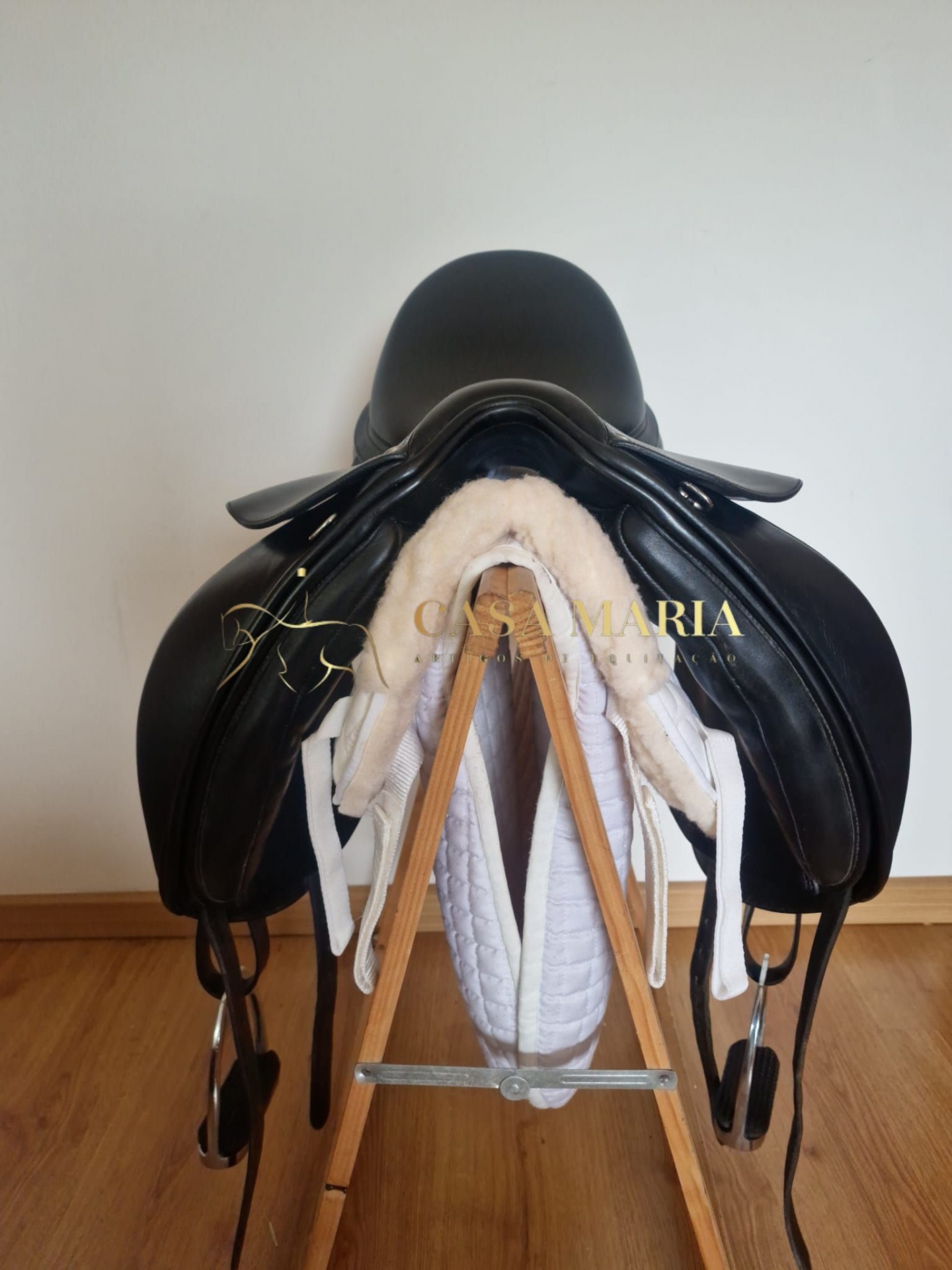 Sela de equitação preta em couro com acolchoado branco num suporte de madeira