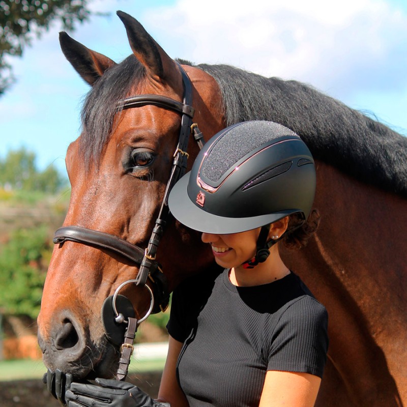 Mulher com capacete preto perto de cavalo castanho com arreio marrom ao ar livre