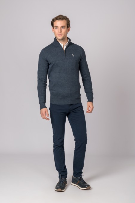 Homem com camisola de malha azul escuro, camisa branca, calças azuis escuras e ténis pretos