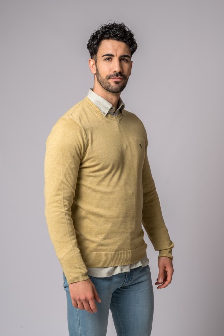 Camisola bege masculina de malha fina com decote em V sobre camisa cinza clara e jeans azuis claros