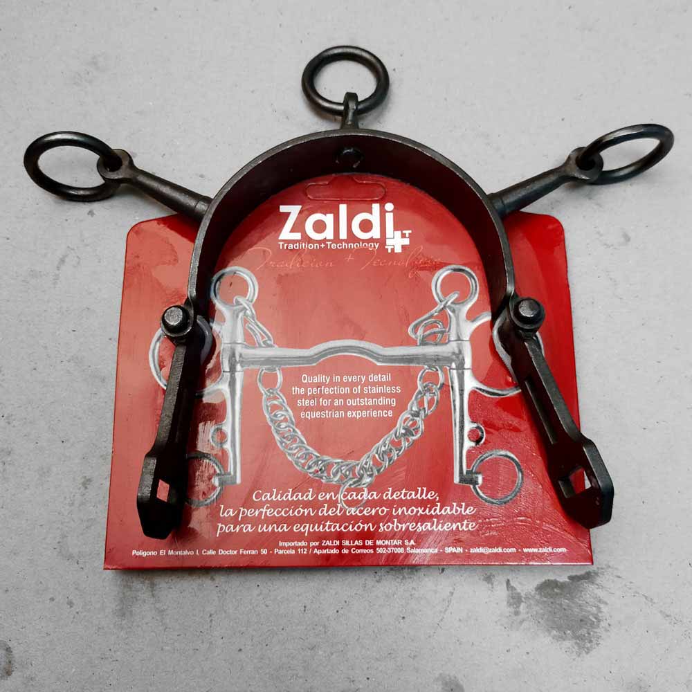 Freio equestre metálico preto com embalagem vermelha da marca Zaldi sobre chão cinzento